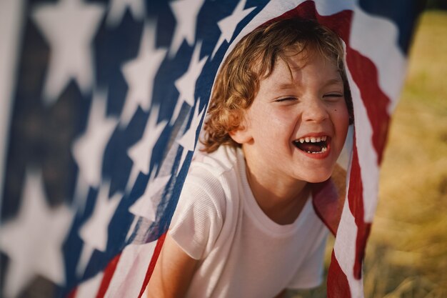 Happy little boy patriot running in the field with American flag. USA celebrate 4th of July