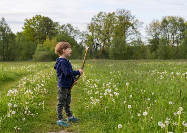 Photo happy little boy playing merrily in nature holds a stick in his hands active lifestyle children outdoors