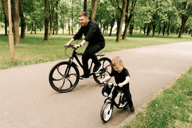 Happy little boy riding a bike with his dad in the park