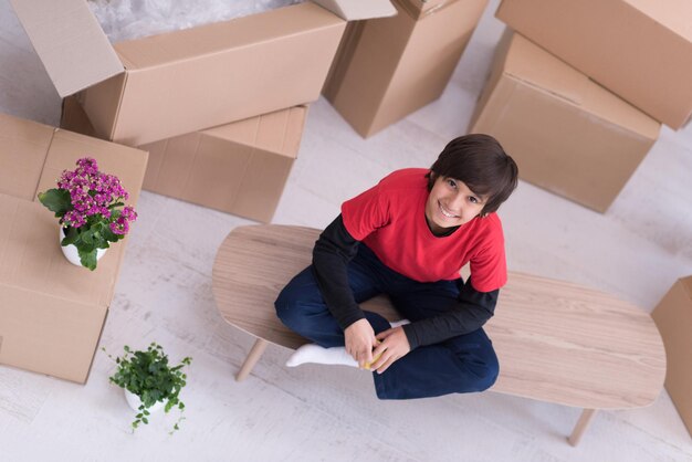 happy little boy sitting on the table with cardboard boxes around him in a new modern home,top view