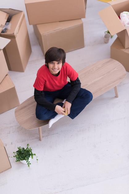 happy little boy sitting on the table with cardboard boxes around him in a new modern home,top view