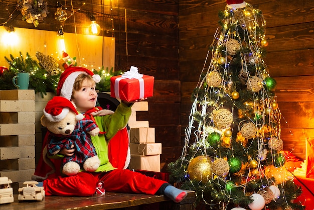 Happy little boy with his Teddy bear and Christmas gift is trying to guess what is inside the gift. Winter, holiday, family time.