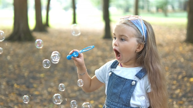 Happy little child girl blowing soap bubbles outside in green park