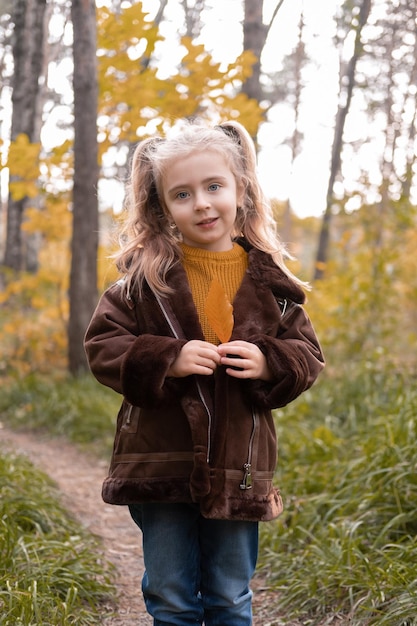 Happy little child girl smiling, holding autumn leaves, having fun in the fall forest