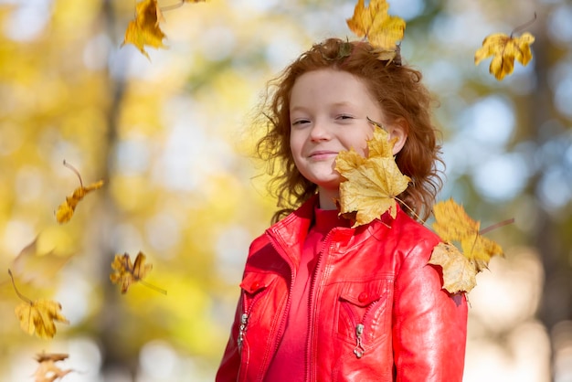 Happy little child redhaired girl laughs and plays with autumn leaves