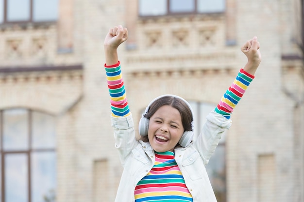 Happy little dreamer positive and colorful child has music break girl in headphones pretty little girl wear wireless headset back to school education with new technology kid sing at schoolyard