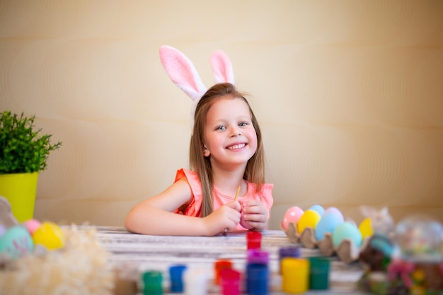 Happy little girl in bunnies ears prepares for easter painted easter eggs happy easter concept