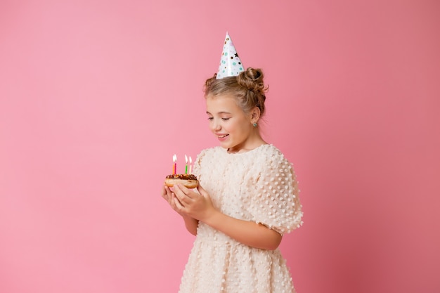 Happy little girl in a cap for her birthday makes a wish and blows out candles on a cake.