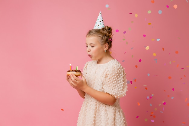 Happy little girl in a cap for her birthday makes a wish and blows out candles on a cake.