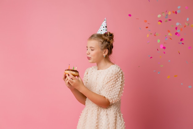 Happy little girl in a cap for her birthday makes a wish and blows out candles on a cake.