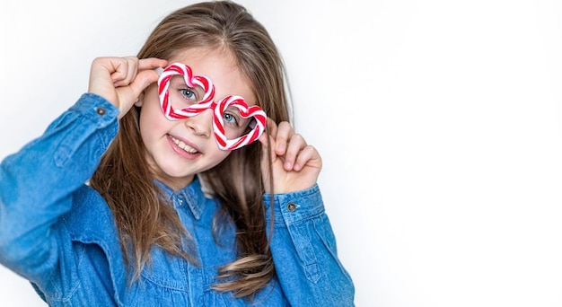 Happy little girl in caramel glasses looks at the camera with hearts and smiles Valentines day background Copy space for text