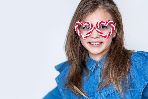 Happy little girl in caramel glasses looks at the camera with hearts and smiles Valentines day background Copy space for text