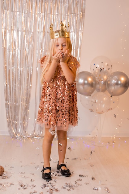 a happy little girl in an elegant dress and a crown blows confetti from her palms and makes a wish.