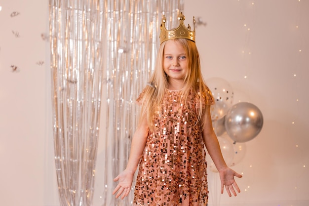 a happy little girl in an elegant dress and a crown blows confetti from her palms and makes a wish.