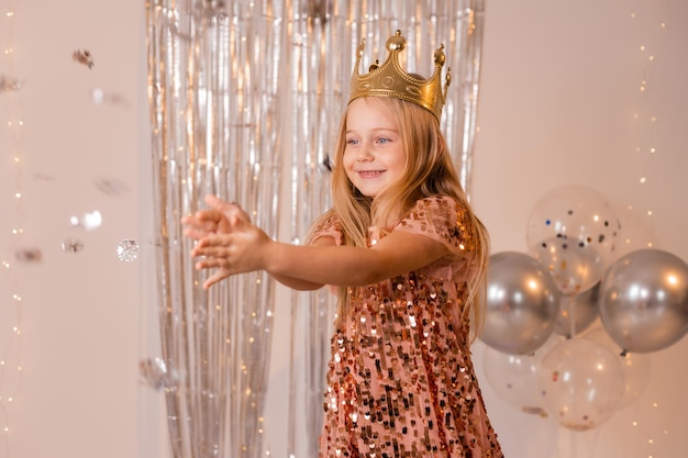 a happy little girl in an elegant dress and a crown blows confetti from her palms and makes a wish.