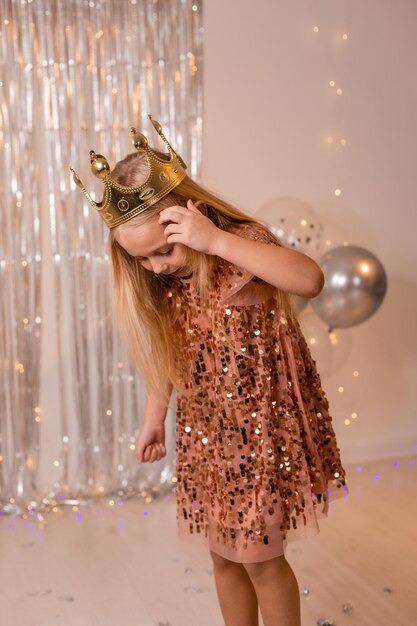 a happy little girl in an elegant dress and a crown blows confetti from her palms and makes a wish.