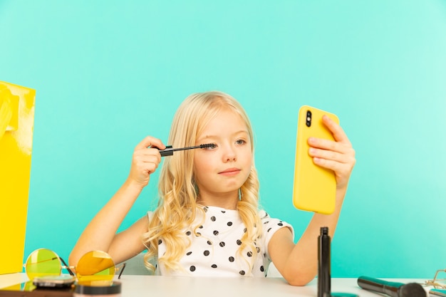 Happy little girl in front of phone camera making video for vlog. Working as blogger, recording video tutorial for Internet.