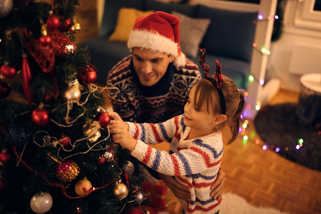 Happy little girl and her father decorating Christmas tree at home