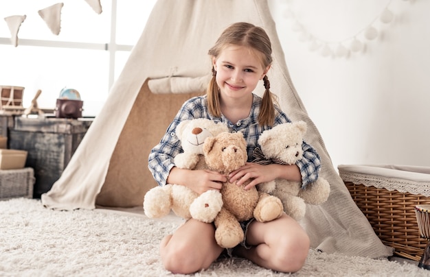 Happy little girl hugging plush bears on wigwam