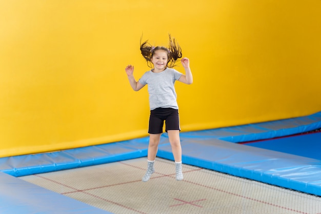 Happy little girl jumping on trampoline in fitness center