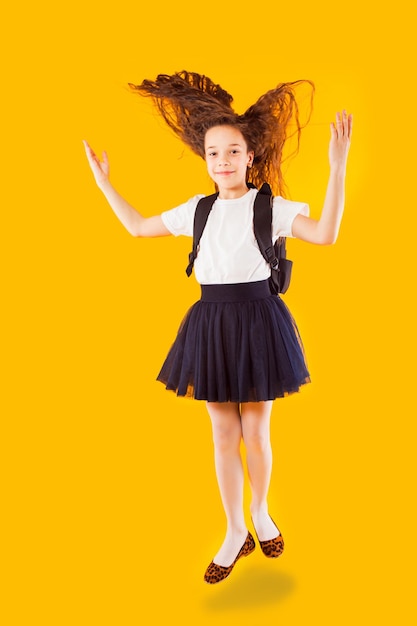 The happy little girl jumps on a yellow background