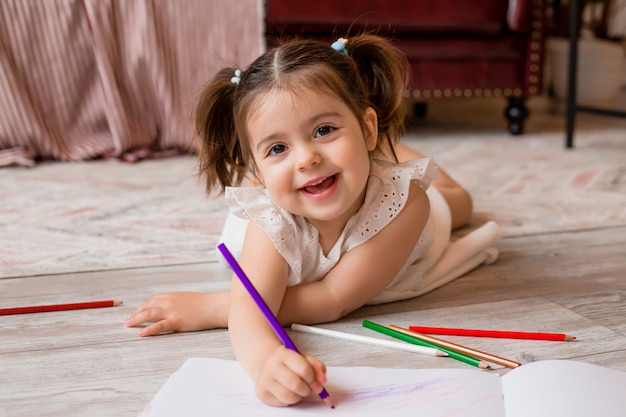 Happy little girl lies on the floor of the house and draws with colored pencils. child's development. Stay at home