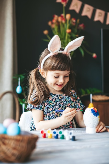 Happy little girl painting Easter egg with paintbrush