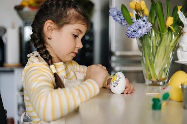 Happy little girl painting easter eggs on kitchen cute smiled girl have fun on spring holiday