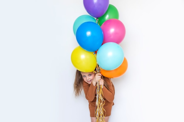 Happy little girl peeks out from behind a bunch of balloons, holding colored balls and laughing merrily. Copy space for text