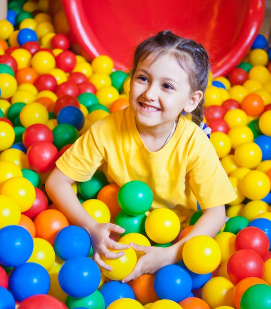 Happy little girl playing in colorful balls. Happy child playing at colorful plastic balls in play center