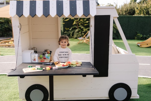 Happy little girl playing on toy kitchen on wheels cute girl make a burger on toy kitchen outdoors