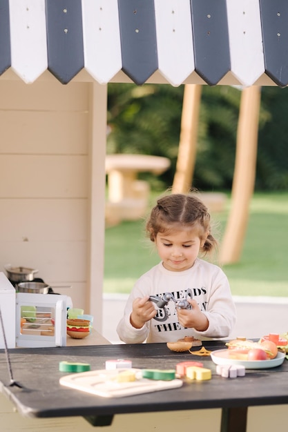 Happy little girl playing on toy kitchen on wheels cute girl make a burger on toy kitchen outdoors