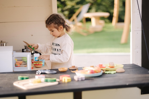 Happy little girl playing on toy kitchen on wheels cute girl make a burger on toy kitchen outdoors