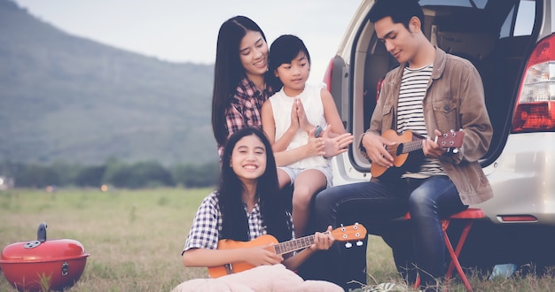 happy little girl playing ukulele with asian family sitting in the car for enjoying road trip and su