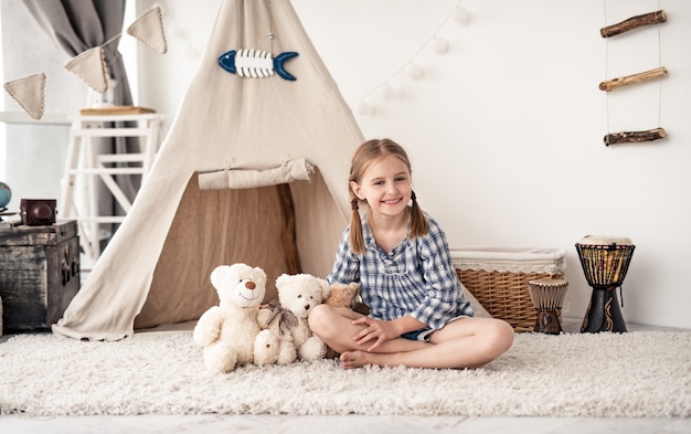 Happy little girl playing with teddy bears in room with wigwam