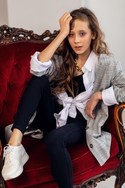 happy little girl portrait little girl in a gray jacket in a crooked interior with a burgundy armchair white sneakers children's fashion happy kids girl model