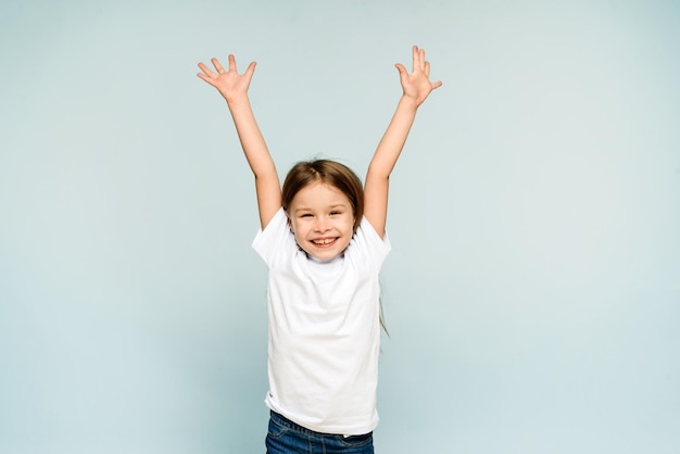 Happy little girl raising her hands up on a blue background with copy space