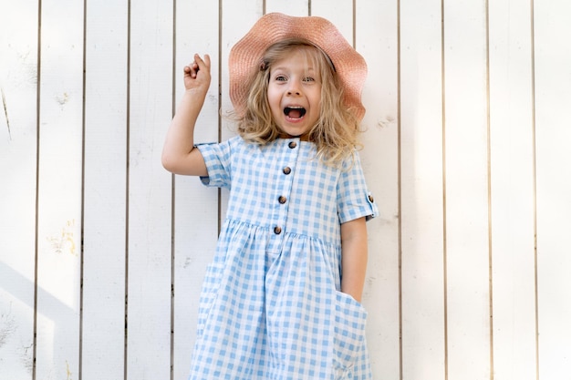 Happy little girl stands by the white wooden wall and smiles