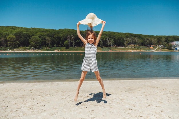 Happy little girl in a straw hat jumping on the beach in summer vacation