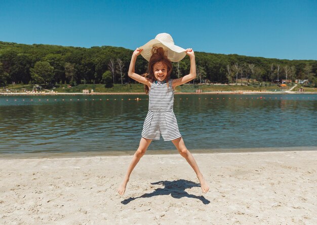 Happy little girl in a straw hat jumping on the beach in summer vacation