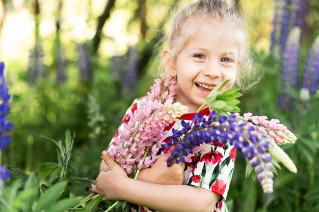 Happy little girl summer in lupin colors, portrait of a blond girl in nature.