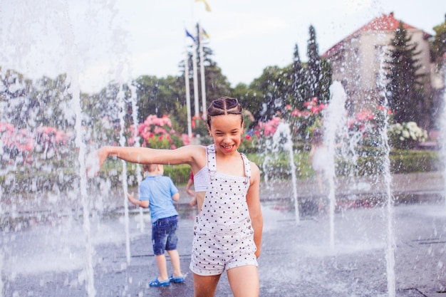 Happy little girl in a wet clothes in the middle of the fountain