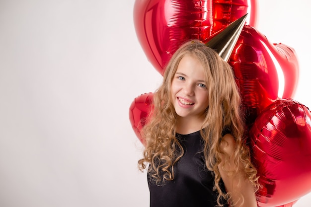 Happy little girl with armful of balls in the form of hearts and a cap for her birthday.