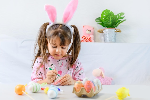 Happy little girl with bunny ears painting the egg with fiberpen preparing for Happy Easter day