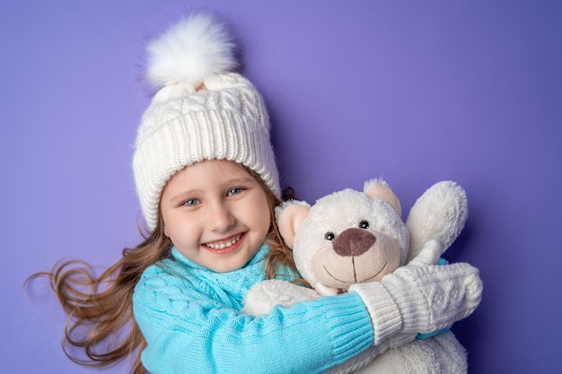 Happy little girl with mittens holding a teddy bear