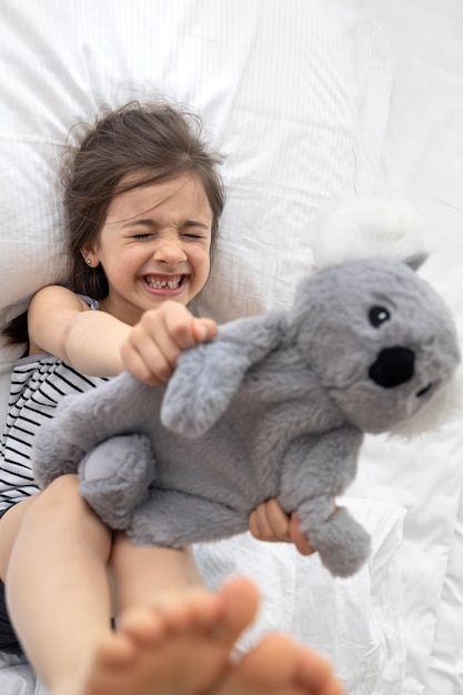 Happy little girl with soft toy koala in bed