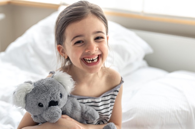 Happy little girl with soft toy koala in bed