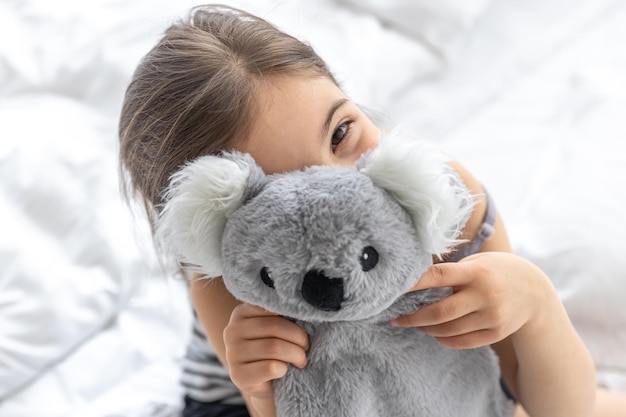 Happy little girl with soft toy koala in bed