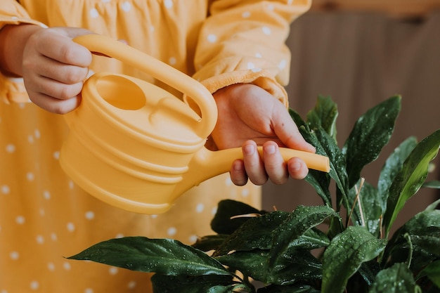 happy little girl in a yellow cotton dress is watering flowers at the dacha. wooden veranda