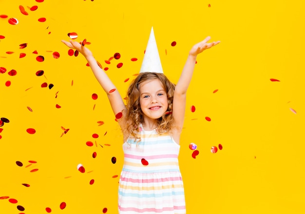 Happy little girl on yellow studio background, copy space. Portrait of a beautiful child having fun with shiny confetti